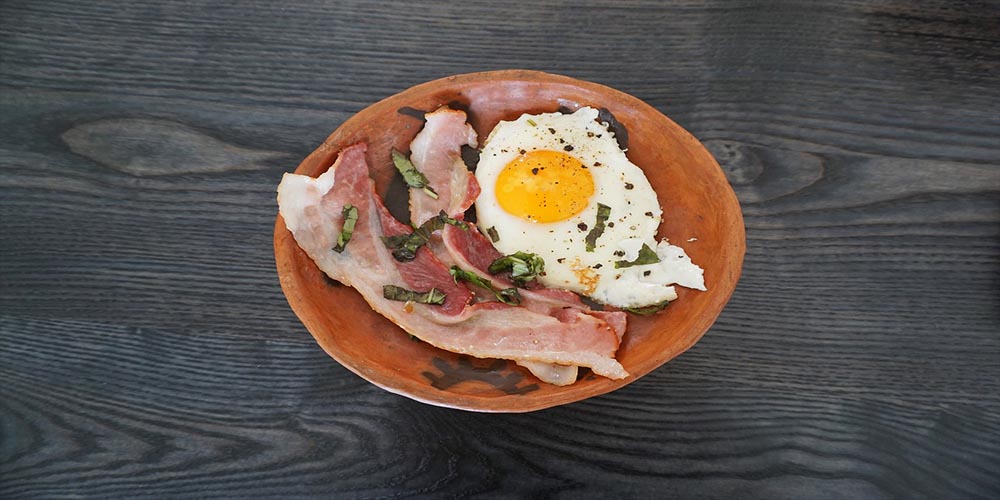 A bowl of bacon and sunny-side up egg garnished with herbs.