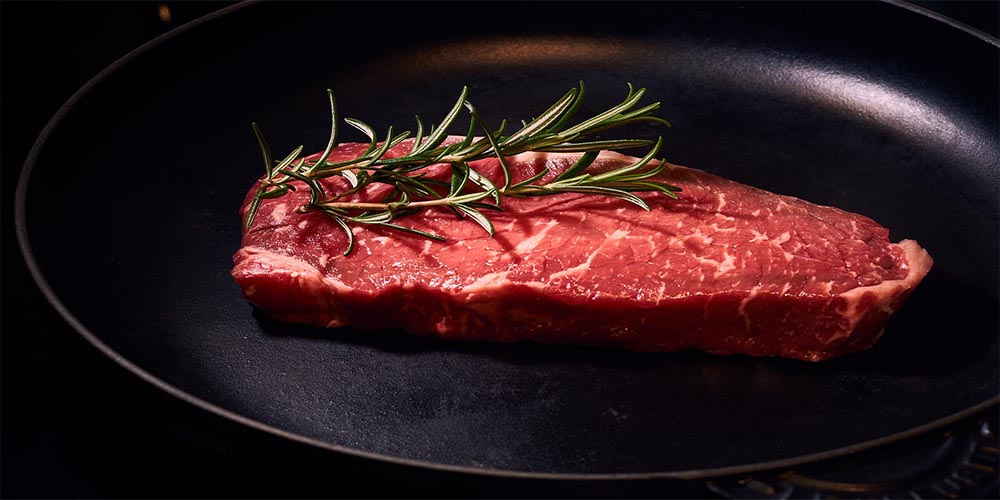 A fresh steak on a pan with rosemary as garnish.