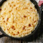 A pan of baked cauliflower mac and cheese on a wooden surface.