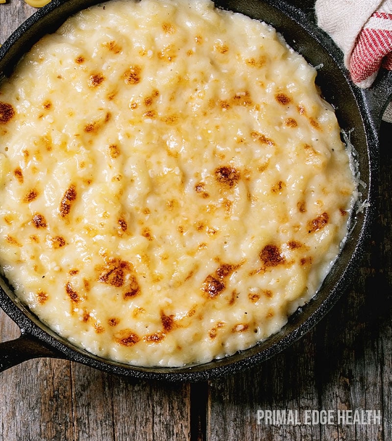 A pan of baked cauliflower mac and cheese on a wooden surface.