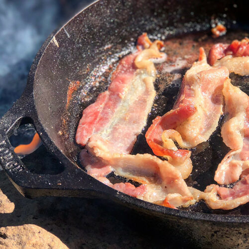 Bacon being cooked in a pan outdoor.