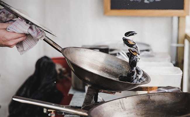 A person holding a pan tossing and cooking shellfish.