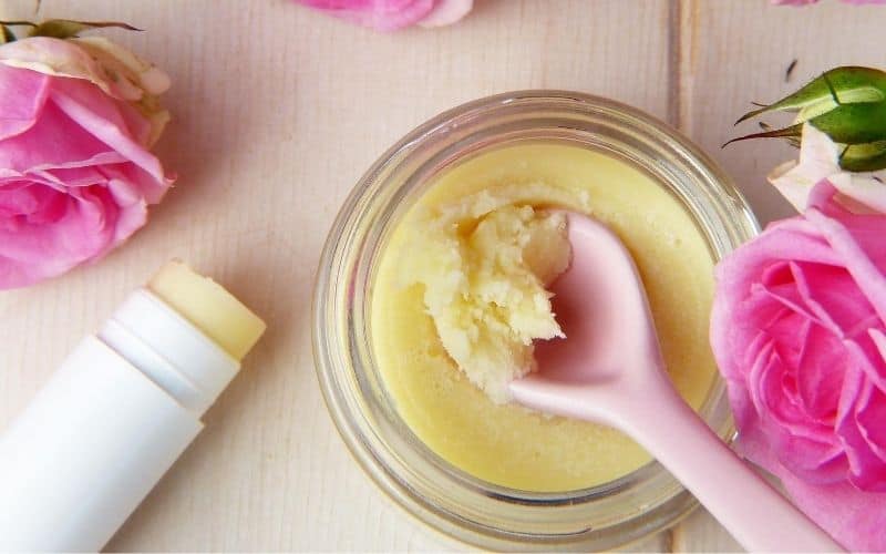 A jar of lip balm with pink roses and a spoon, providing a soothing and nourishing solution for lip care.