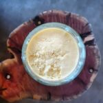 A jar of beef tallow on top of a wooden cutting board.