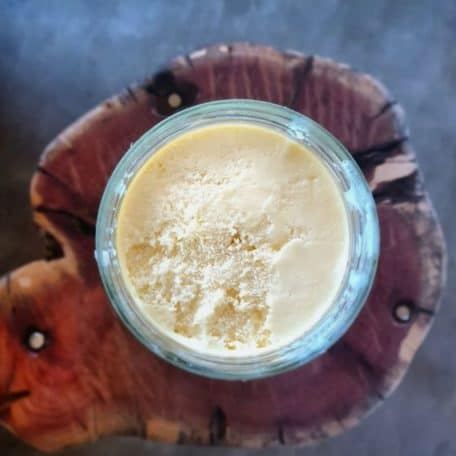 A jar of beef tallow on top of a wooden cutting board.