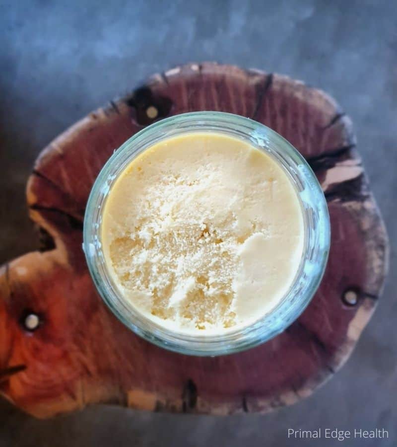 A jar of beef tallow on top of a wooden cutting board.