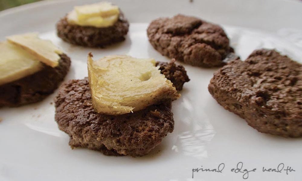 Four homemade cookies topped with slices of butter are displayed on a white plate, their richness reminiscent of primal edge health. The name "primal edge health" is written at the bottom right corner of the image, subtly nodding to the wholesome, nutrient-dense benefits akin to beef heart.