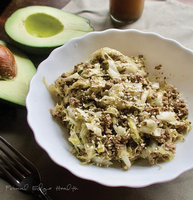 A plate of cabbage noodles and ground beef with avocados in the background.