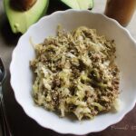 A serving of cabbage noodles with beef in a white bowl on a wooden surface.