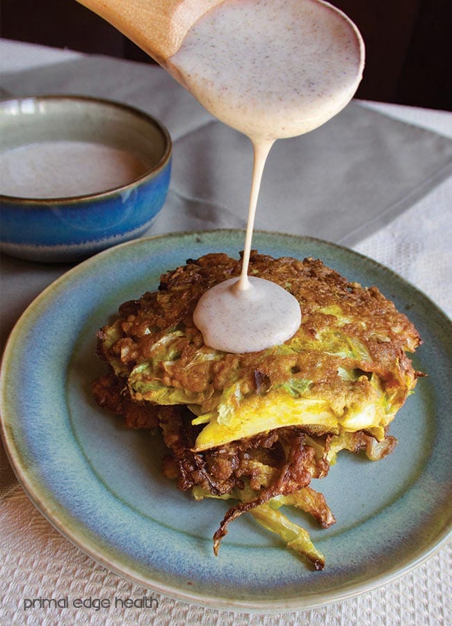 Cabbage pancakes on a plate with yogurt sauce being drizzled on it.