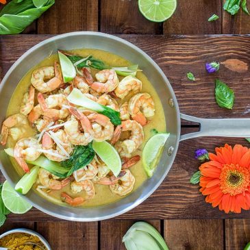 Shrimp dish in a pan surrounded by flowers and green leaves.