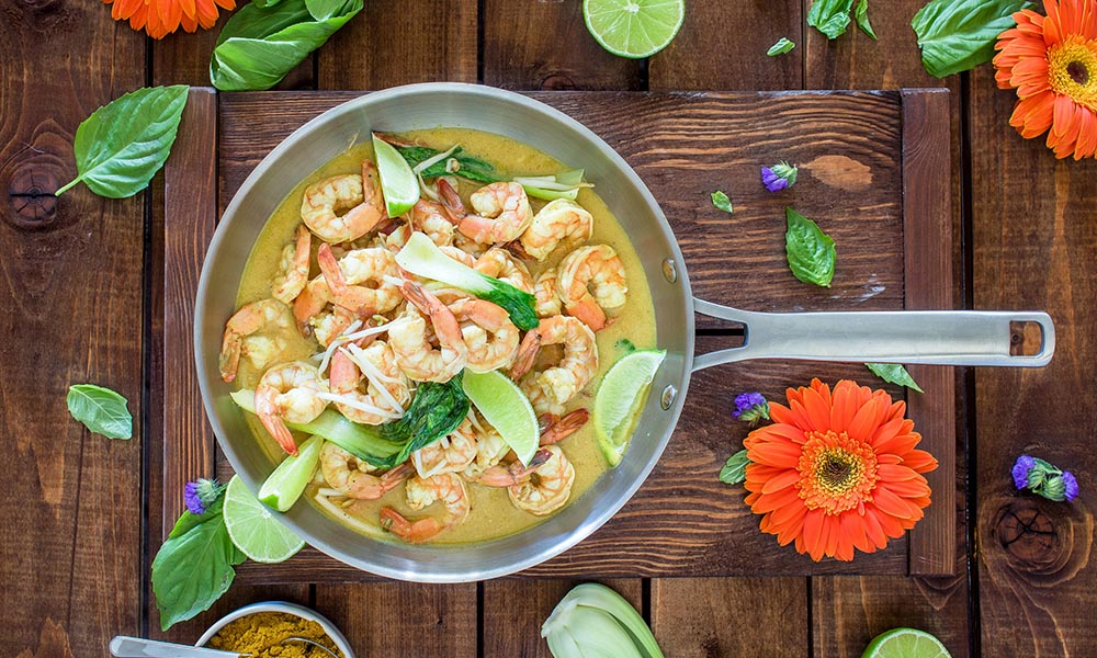 Shrimp dish in a pan surrounded by flowers and green leaves.