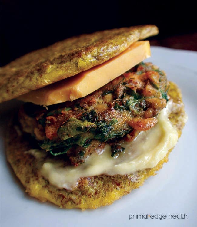 Spinach and salmon burger with cheese on a white plate.