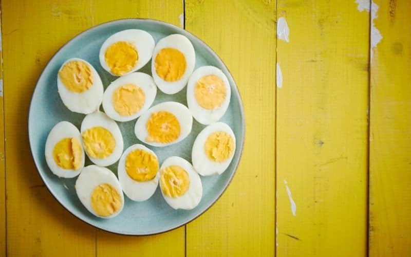 A batch of boiled eggs cut in half on a yellow wooden surface.