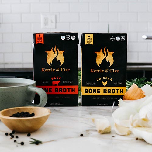 Fire and kettle chicken and beef bone broth on the countertop with onion, garlic and peppercorns.