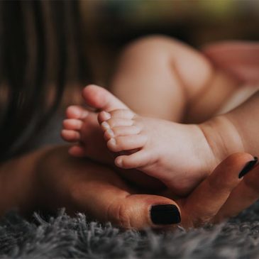 A woman's gentle hand carefully cradles a newborn baby's tiny foot, radiating love and tenderness.