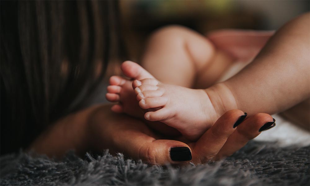 A woman's gentle hand carefully cradles a newborn baby's tiny foot, radiating love and tenderness.
