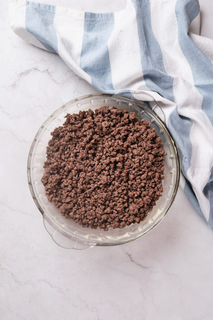 Cooked ground beef in a clear glass bowl on a marble countertop.