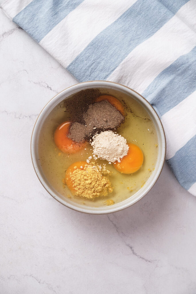 Bowl containing eggs and other spices on a white and blue striped towel.