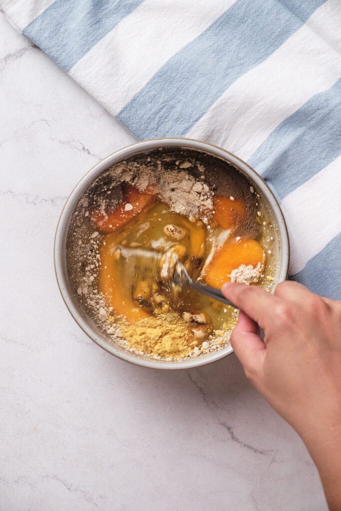 A person's hand mixes eggs, flour, and spices.