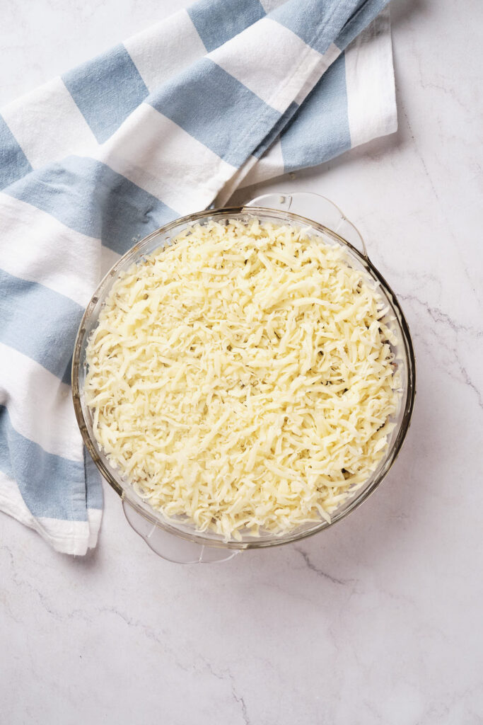 A glass dish filled with shredded cheese for cheeseburger pie.