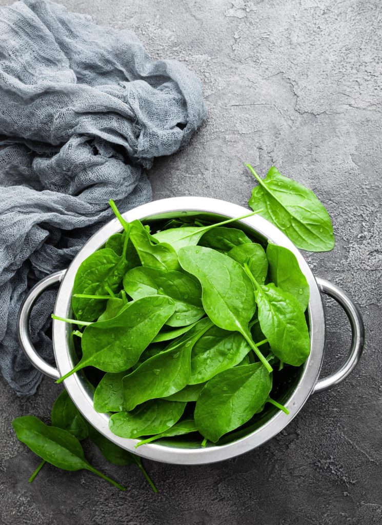 A bowl of leafy greens on a grey surface.