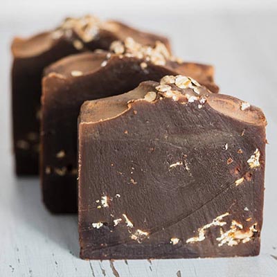Three bars of chocolate soap with oats on top, made using cold process soap making.