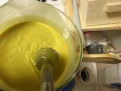 A bowl of yellow liquid with a spoon in it, perfect for beginners learning to make cold process soap.