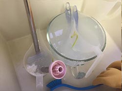 A sink with a bowl of water and a pair of gloves, perfect for a beginner's cold process soap recipe.