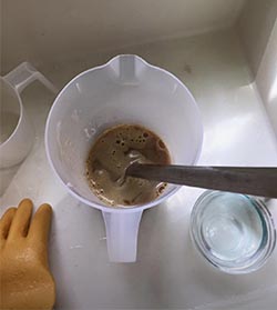 A cup of liquid soap and a pair of gloves on a sink.