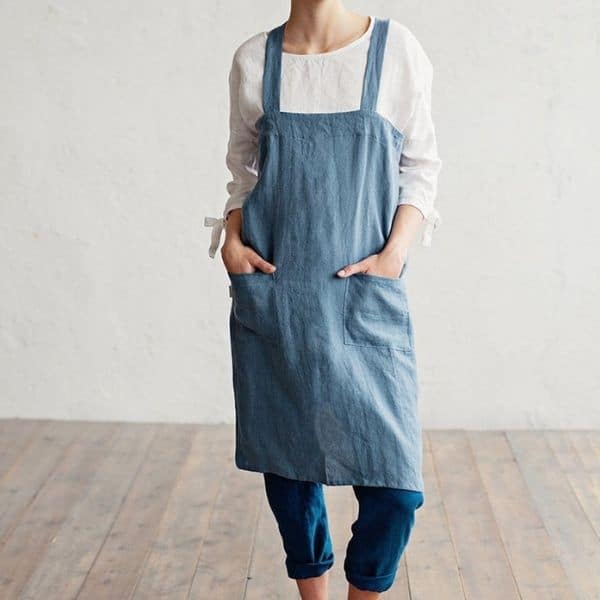 A person wearing a blue apron and white long sleeve shirt.
