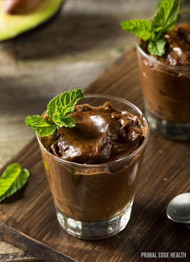 Two servings of keto chocolate avocado pudding on a wooden surface.