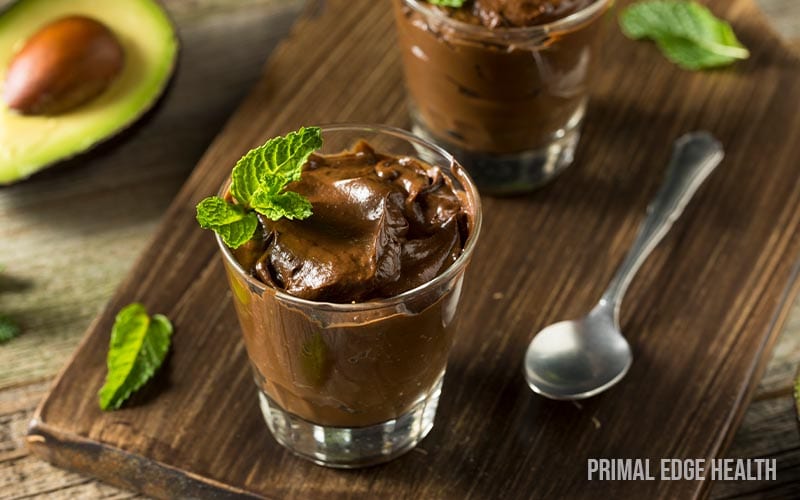Two glasses of keto chocolate avocado pudding on a wooden surface.