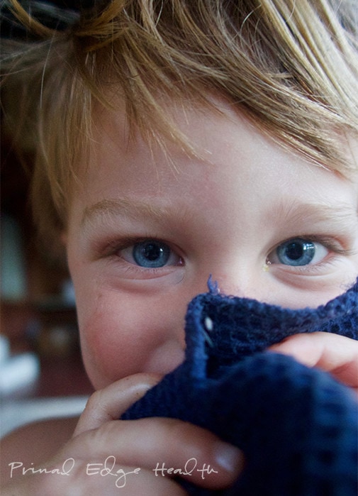 A young boy with blue eyes peeking out of a towel.