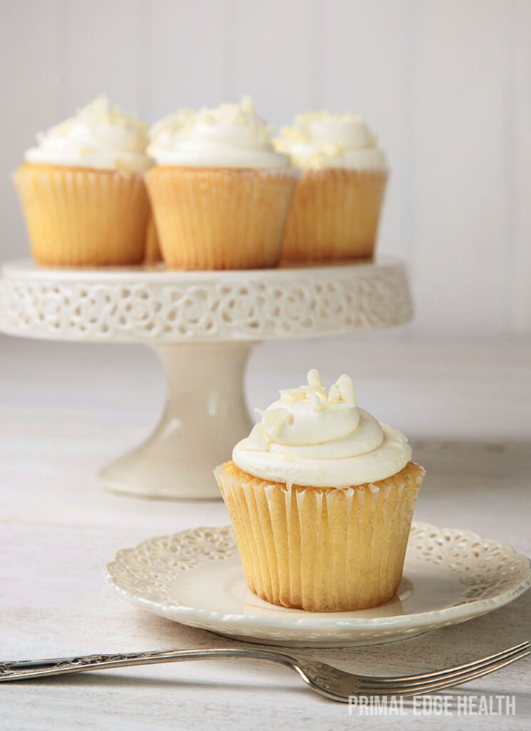 A batch of vanilla cupcakes on a round stand and one on a white plate.