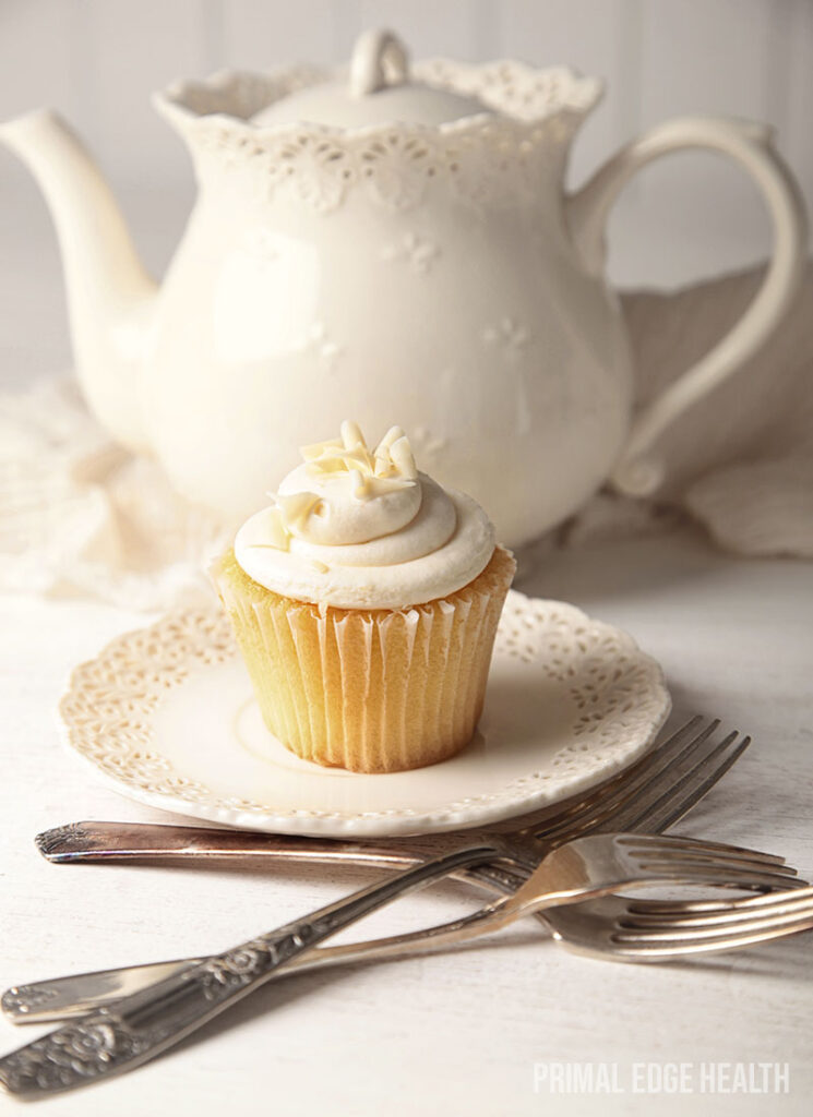 Vanilla cupcake on a white plate and a white teapot in the background.
