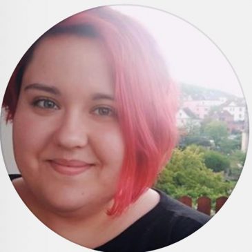 A woman with red hair smiling in a black shirt.