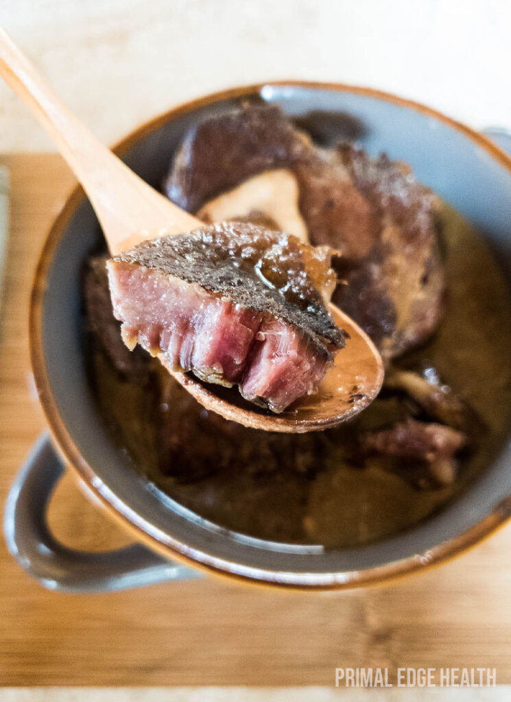 Spoonful of braised beef on wooden spoon, over bowl.