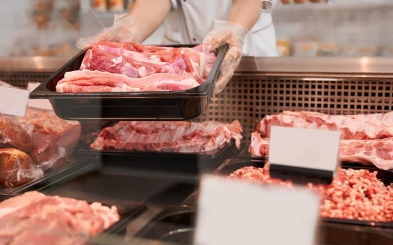 A person is organizing meat trays in a store.
