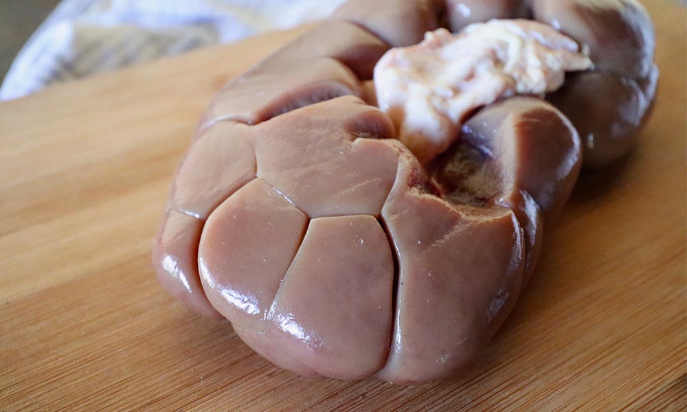 Raw beef kidney on a wooden board.