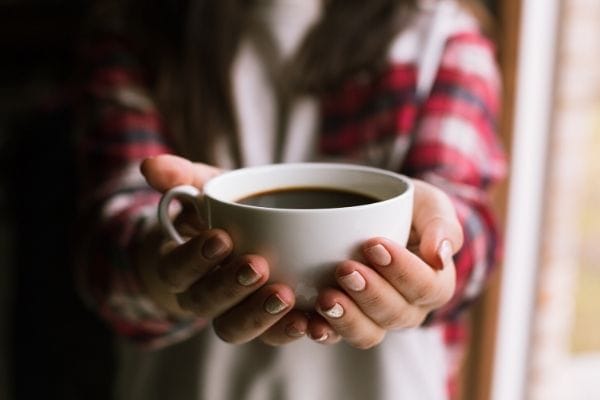 A woman holding a cup of coffee with both hands.