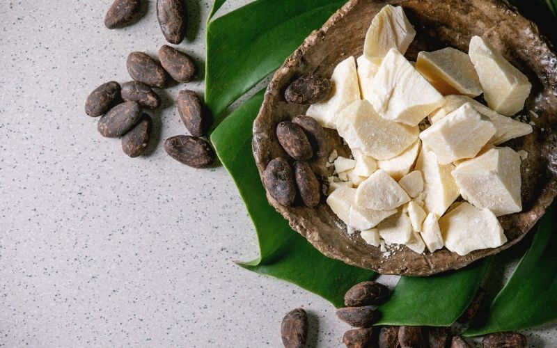 Keto-friendly cocoa butter and cocoa beans displayed in a bowl on a white background.