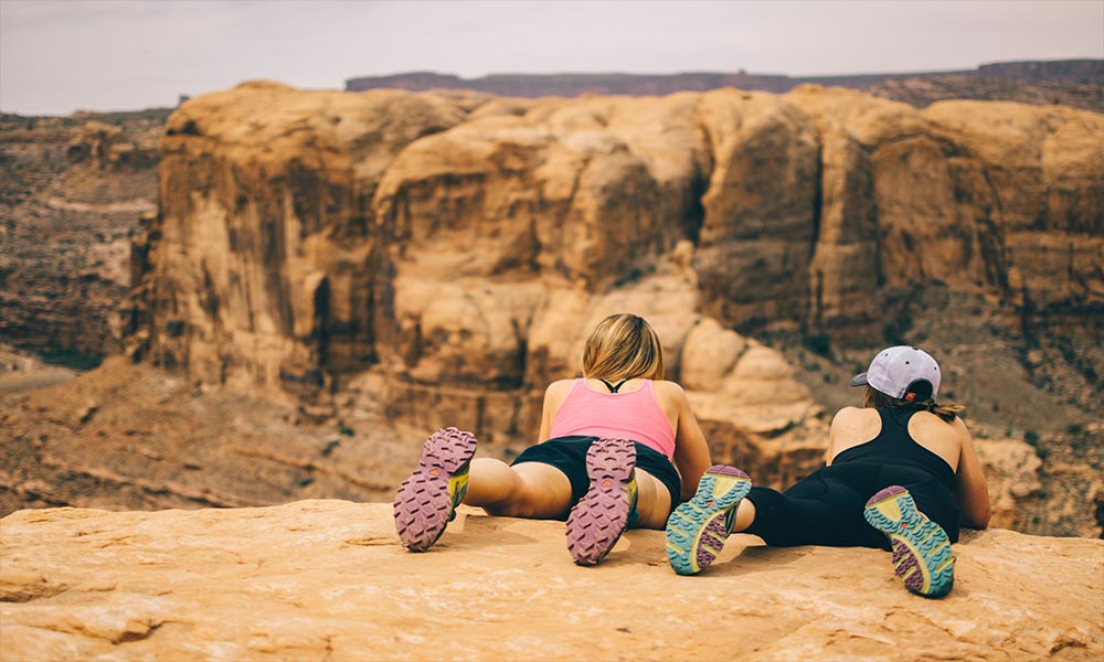 Two women sitting on top of a cliff overlooking a canyon.