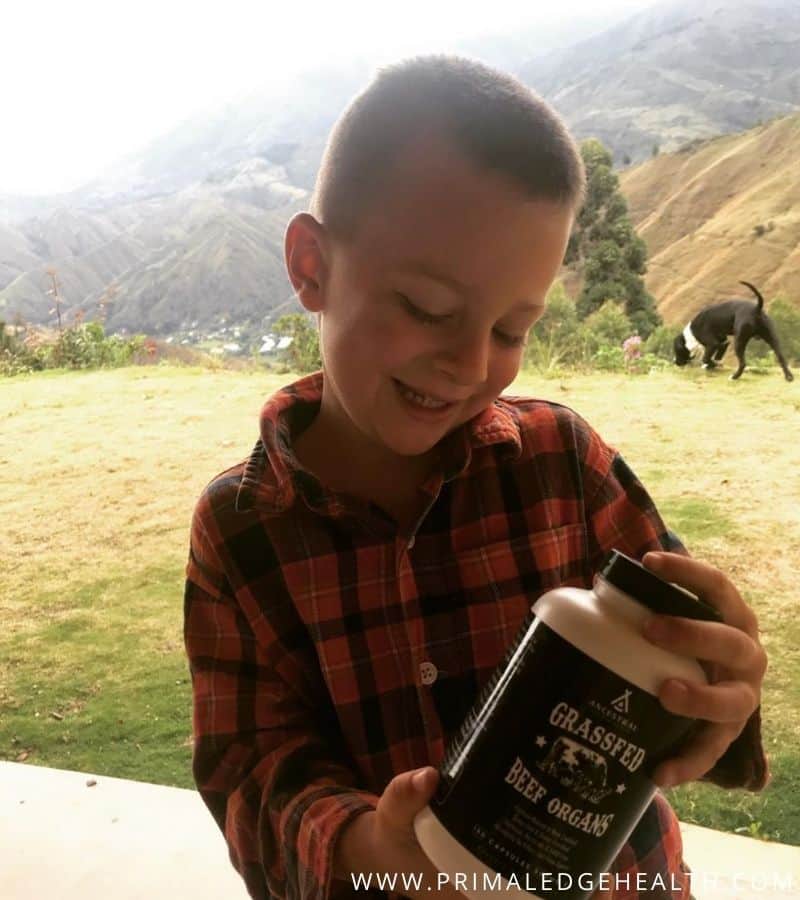 A smiling boy holding a black and white supplement bottle.