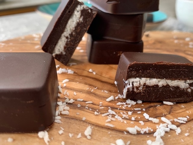 Keto chocolate coconut squares on a wooden cutting board.