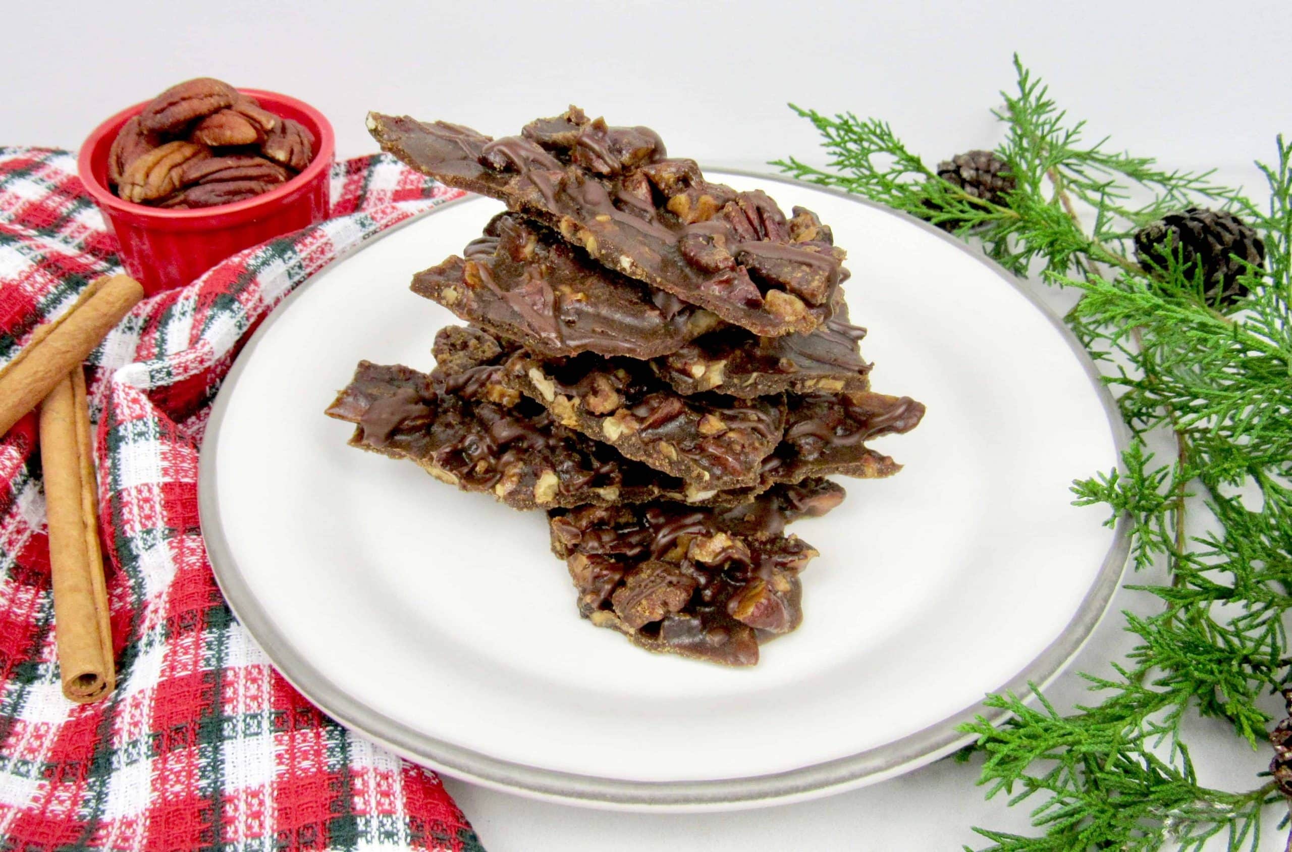 Pecan brittle on a plate with cinnamon sticks.