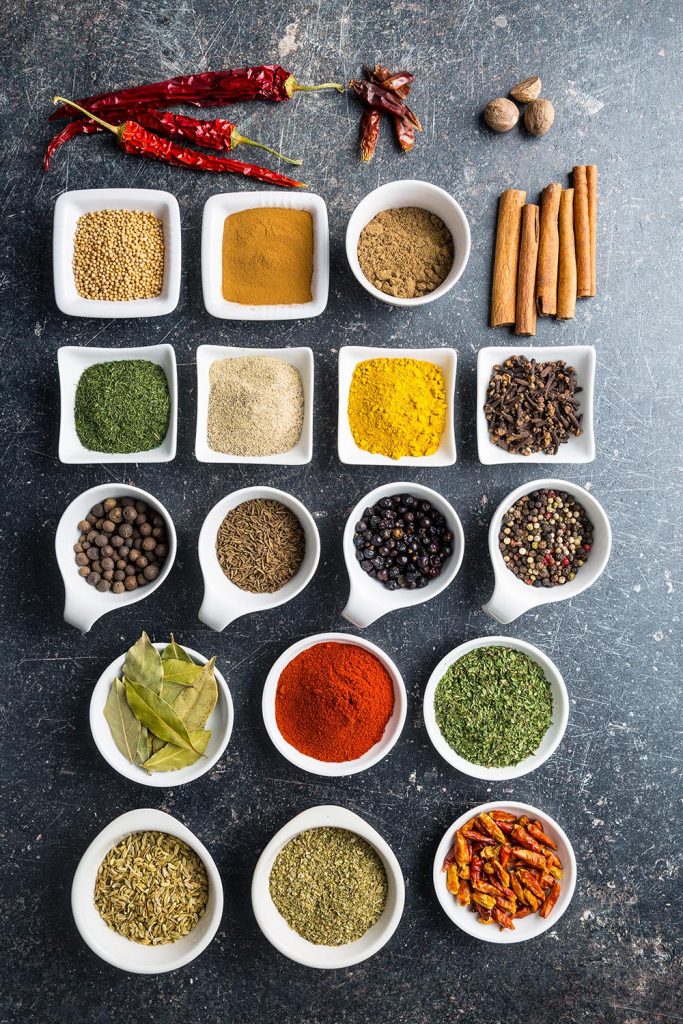 A variety of spices in white bowls on a dark background.
