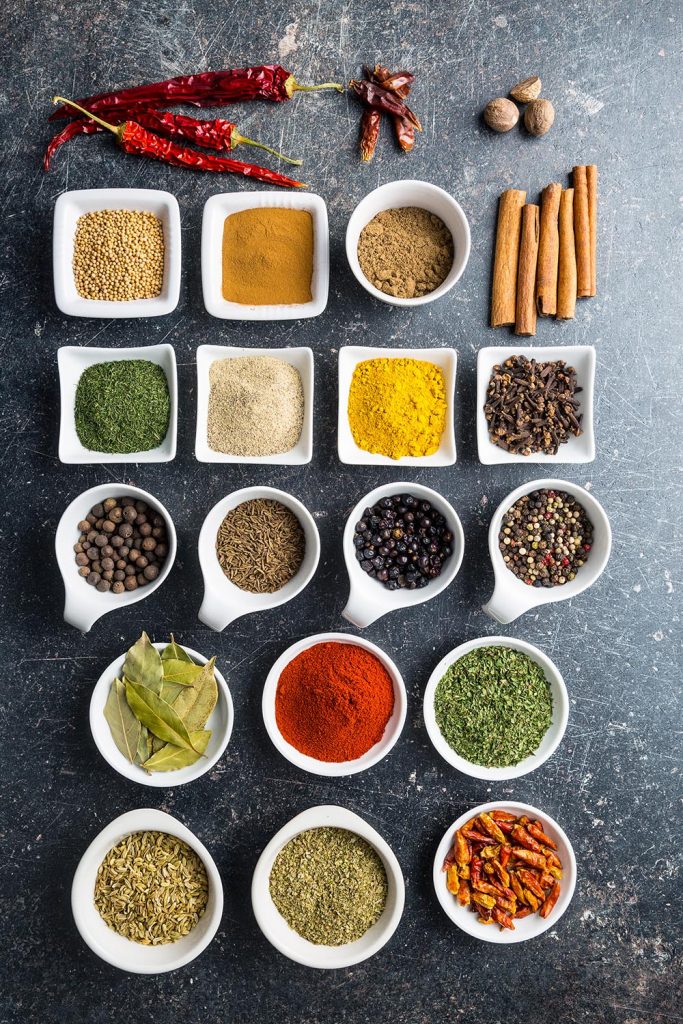 A mountain rose herbs review of a variety of spices in white bowls on a dark background.