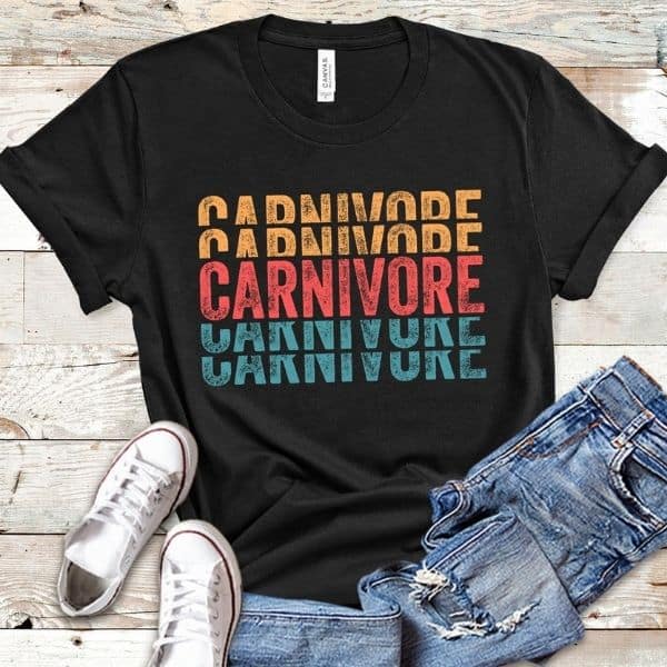 Black shirt with "Carnivore" written on it, jeans, and white shoes on a wooden surface.