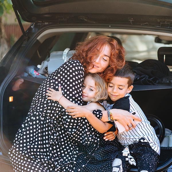 A woman and two children hugging in the trunk of a car.